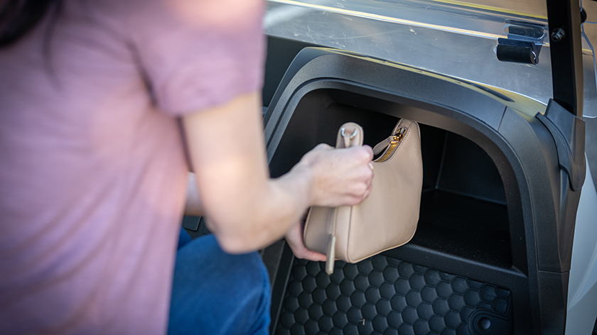 An E-Z-GO passenger using dashboard storage to hold their bag.