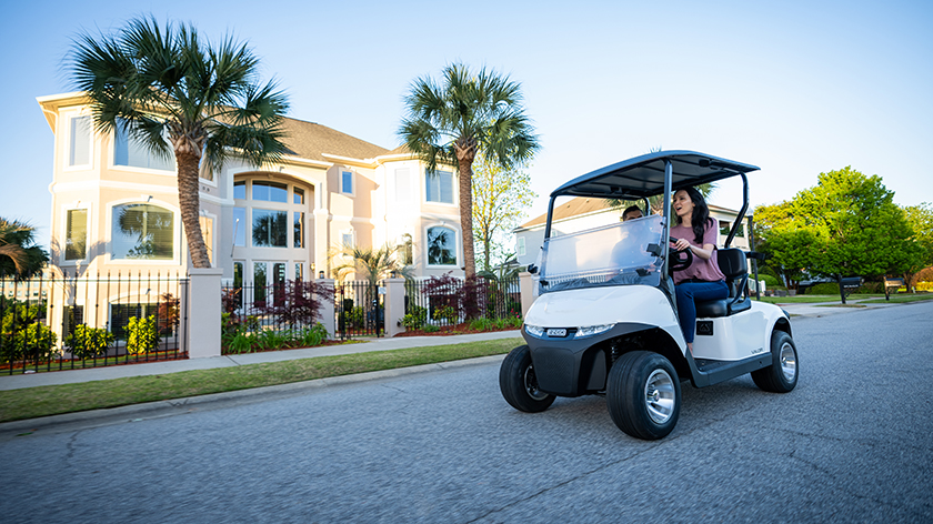 A woman drives an E-Z-GO Valor model down an empty road.