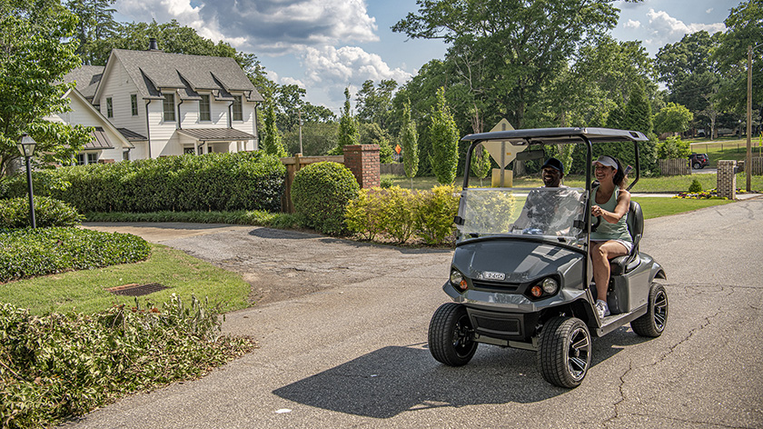 A couple driving an E-Z-GO Express S2 down a neighborhood street.