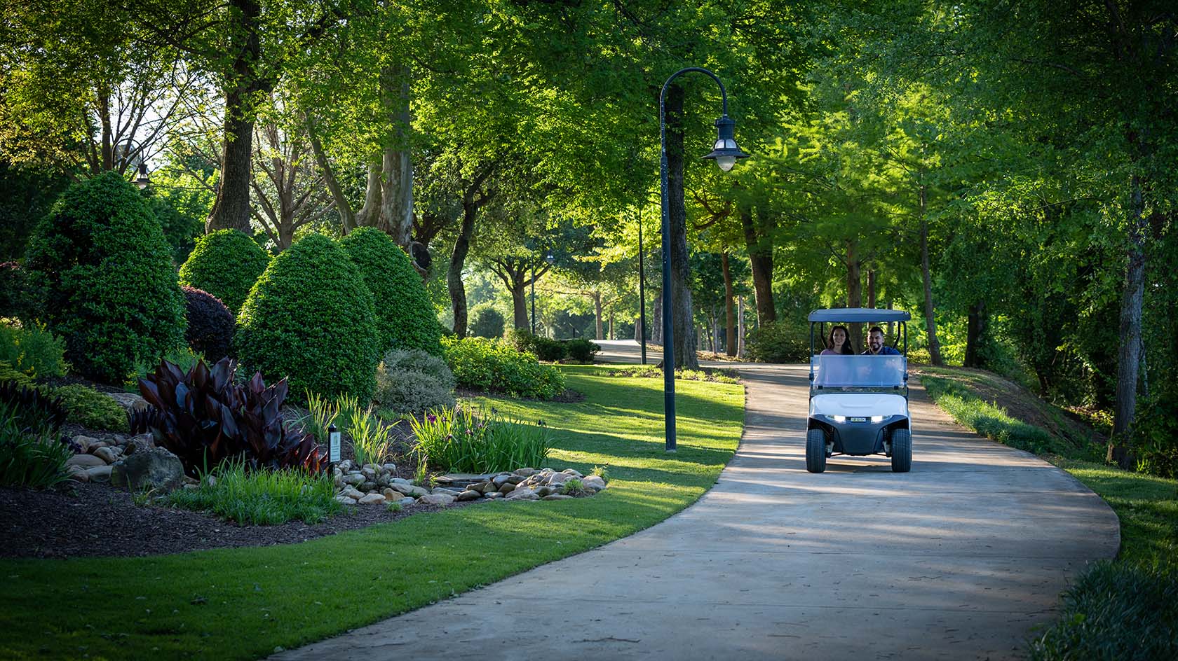 A woman and man ride an E-Z-GO Valor model down a winding path.