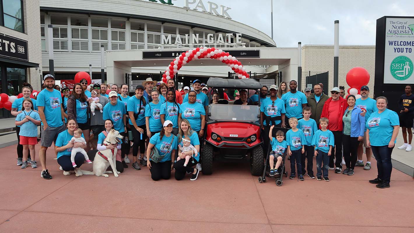 A large group of E-Z-GO affiliates wearing blue shirts surround a red E-Z-GO golf cart.