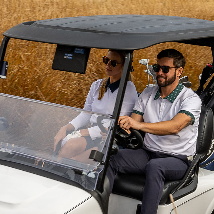 Two riders drive an E-Z-GO through a field.