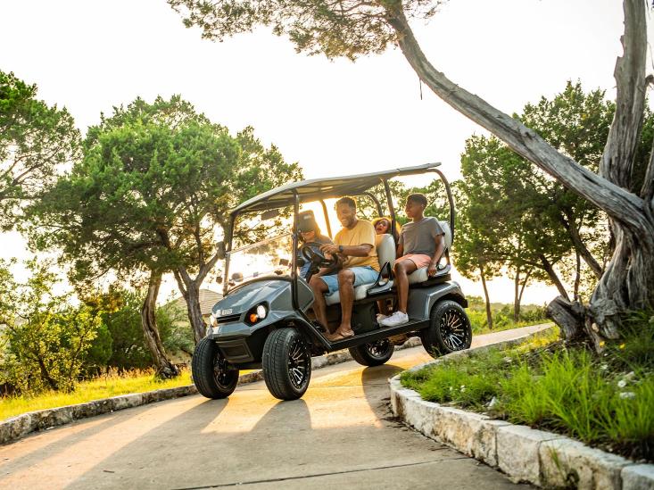 A group of friends drive in their E-Z-GO down a paved path.